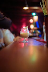 A vibrant cocktail on a bar counter with colorful lighting and lively atmosphere.